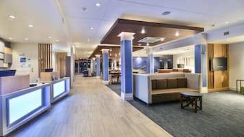 Un moderno vestíbulo de hotel con mostrador de recepción, zona de estar y televisor.