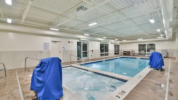 Una piscina interior con agua cristalina, bordes de azulejos y una zona techada con una silla para socorrista.
