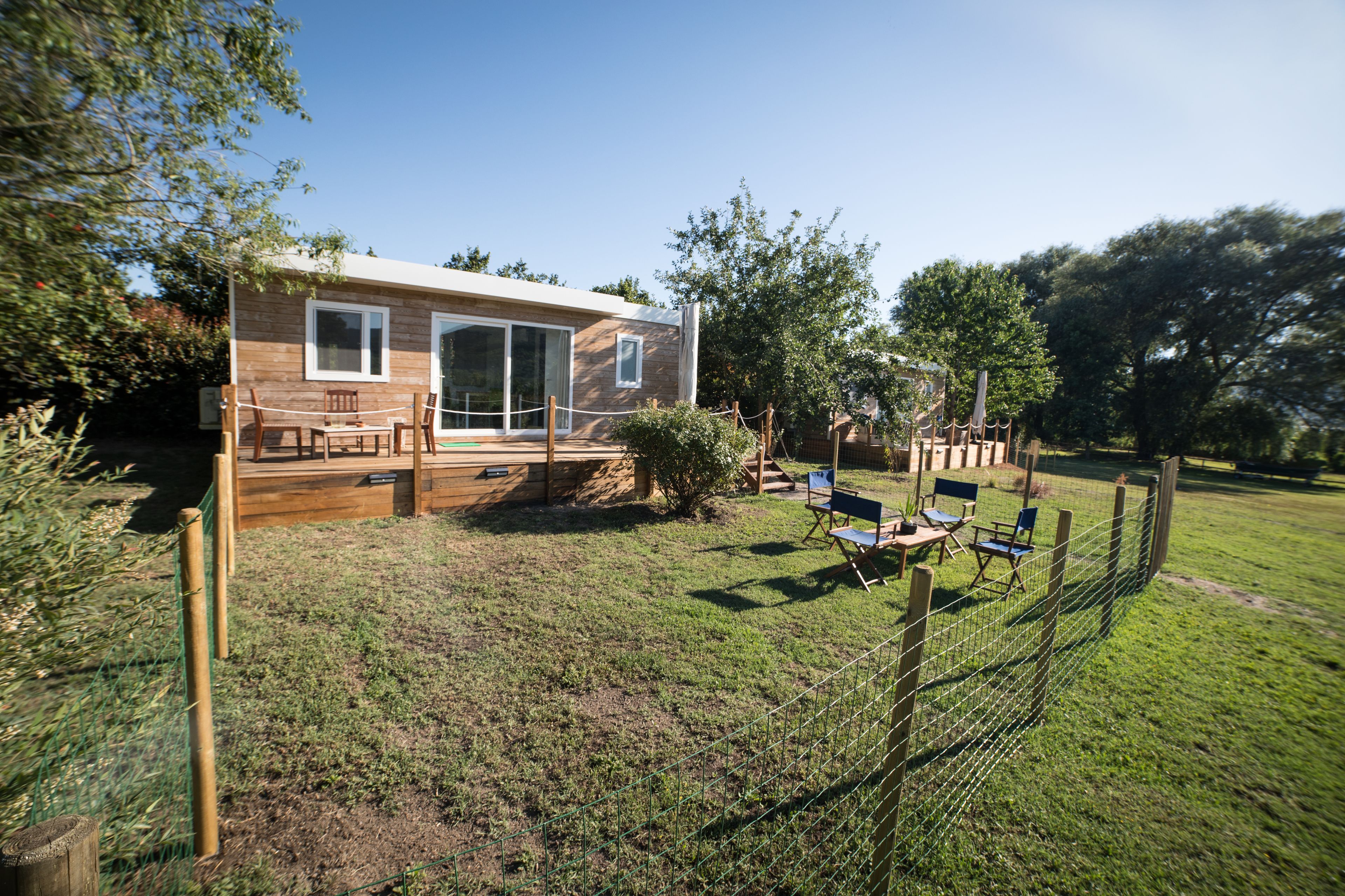 A wooden house with a deck, outdoor seating, and a fenced yard.
