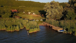 Une vue sur la rivière, avec une jetée en bois, un petit bateau et une zone herbeuse, des bâtiments se dressant à l’arrière-plan.
