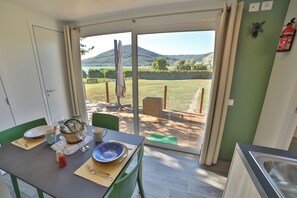 A dining area with a table set for two, a view of a garden and mountains through a glass door, and a fire extinguisher on the wall. - Cottage Beach Vico (Caprarola)