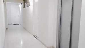 A long, narrow hallway with white walls and a tiled floor. There are doors on both sides, one of which has a sliding door. - Departamentos Monterrico (Santiago de Surco)
