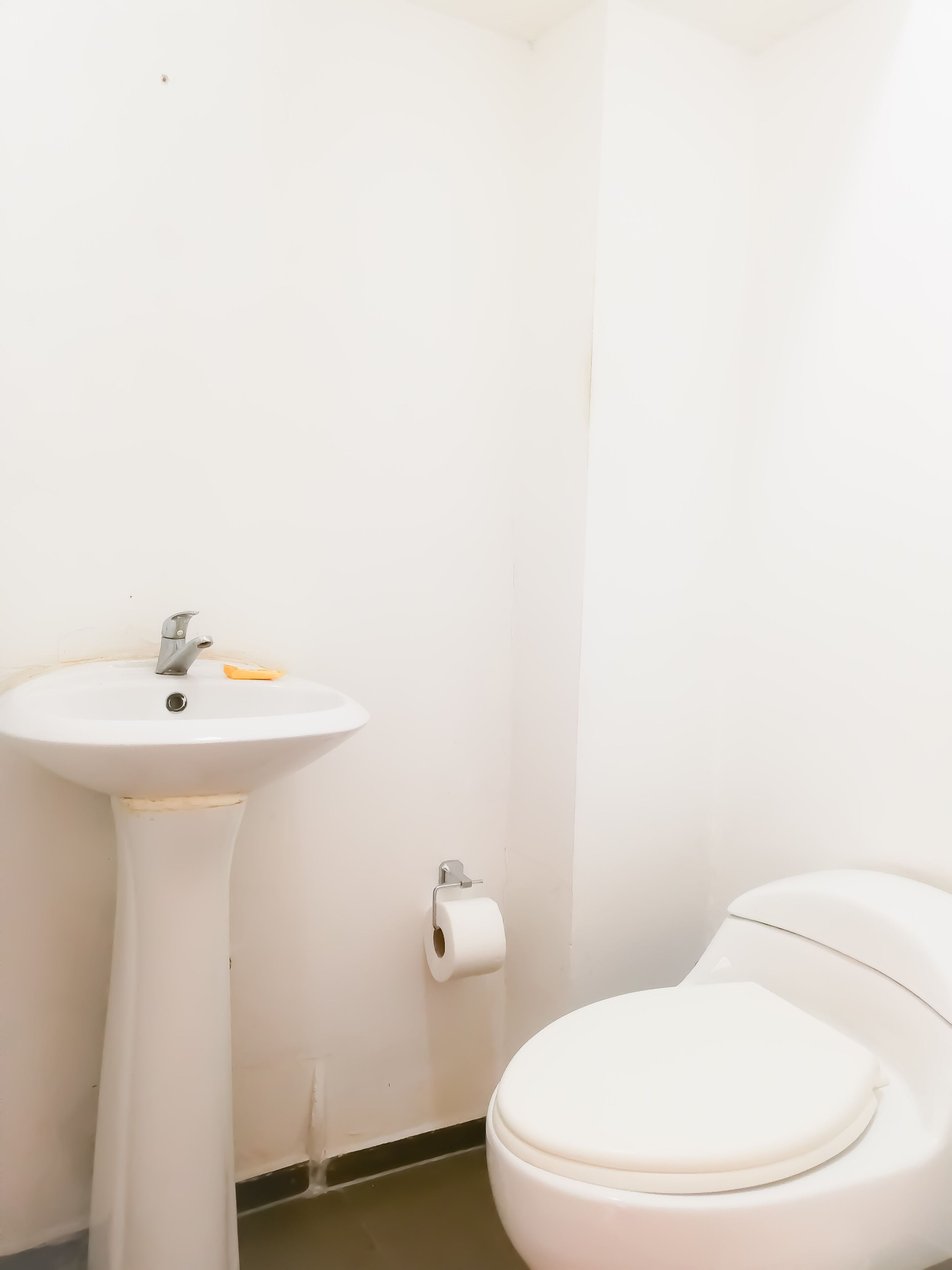 A small, white bathroom with a pedestal sink, toilet, and a toilet paper holder on the wall.