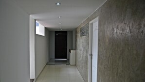A narrow hallway with a tiled floor, a door at the end, and a window on the left wall. - Departamentos Monterrico (Santiago de Surco)