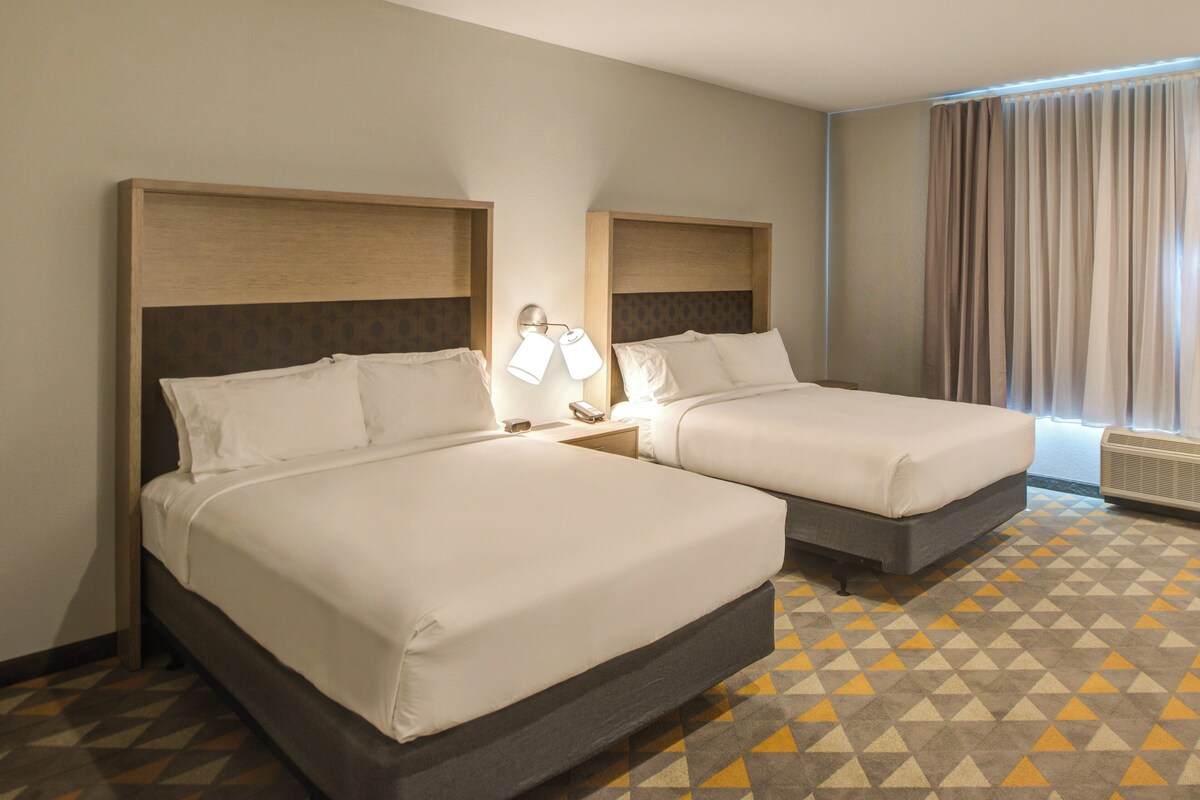 A hotel room with two beds, a patterned floor, and a window with curtains.