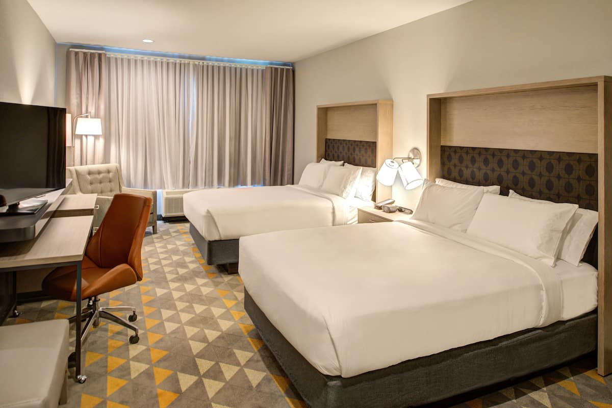 Une chambre d’hôtel avec deux lits, un bureau avec une chaise, une télévision et une grande fenêtre avec des rideaux.