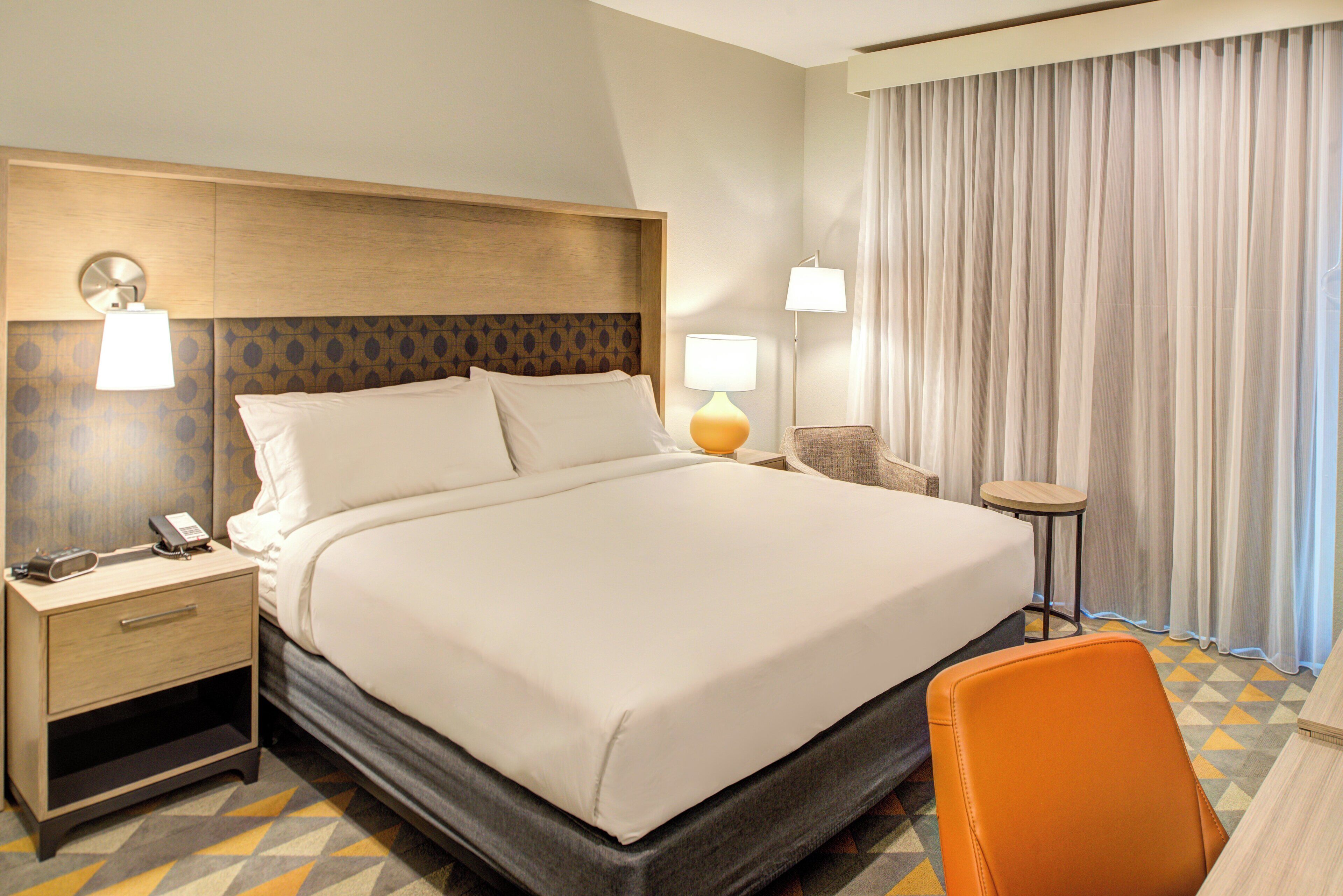 A hotel room with a large bed, bedside tables, a chair, and a lamp.