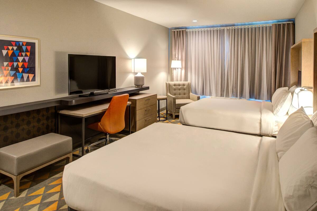 Une chambre d’hôtel avec deux lits, un bureau avec une télévision, une chaise, une lampe et un tableau au mur.