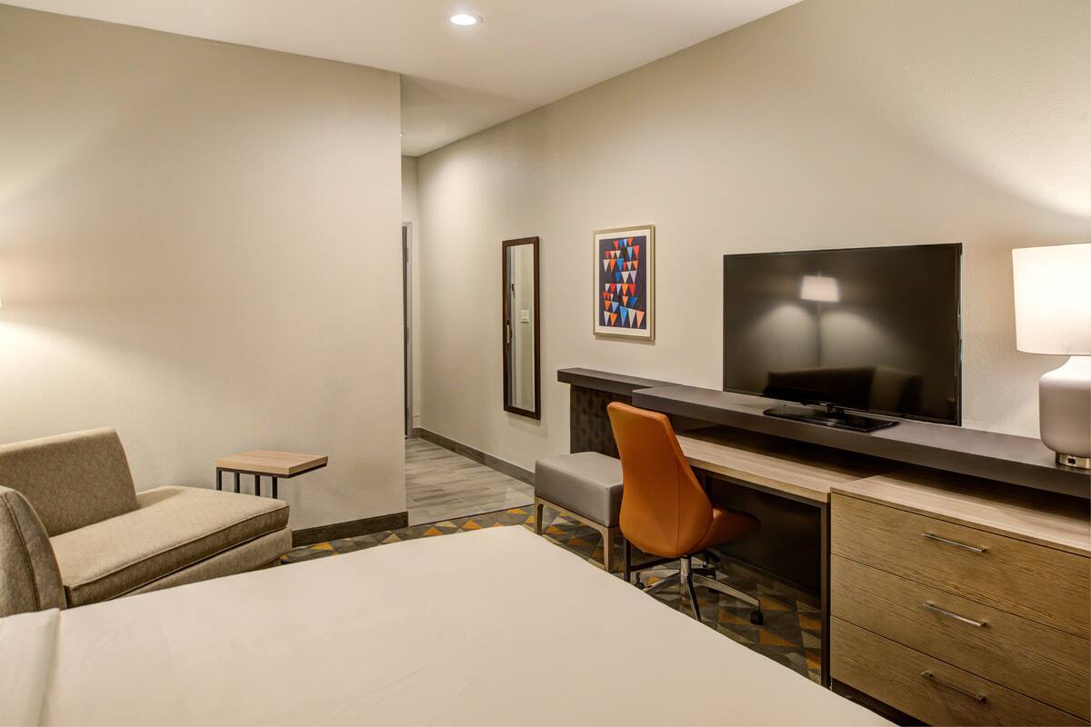 Une chambre d’hôtel avec un lit, un bureau, une chaise, une télévision et une petite table.