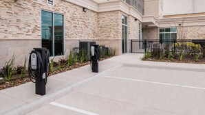 A parking area with electric vehicle charging stations, a building with a stone facade, and a clear sky.