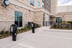 A parking area with electric vehicle charging stations, a building with a stone facade, and a clear sky.