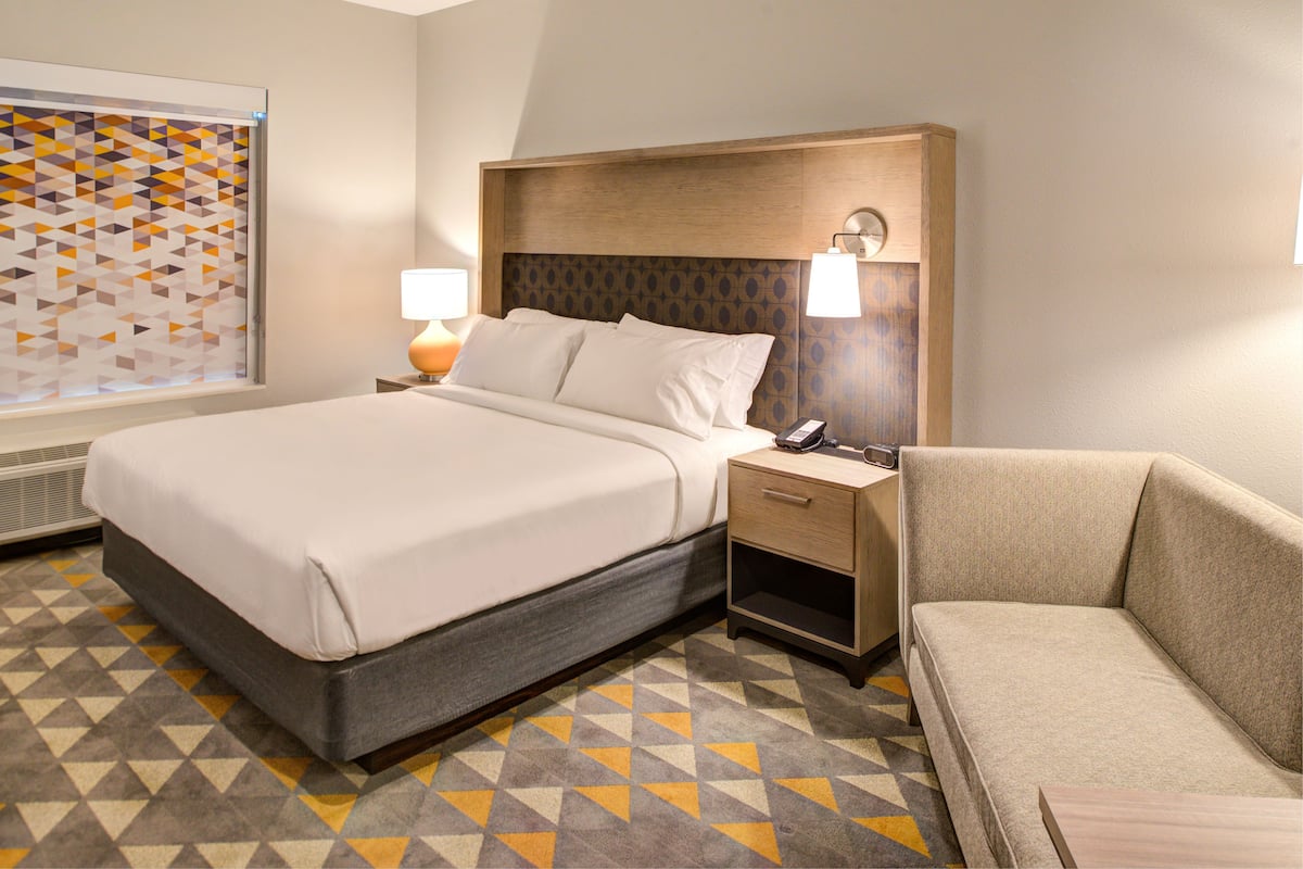 Une chambre d’hôtel avec un lit, une table de chevet, une lampe et un canapé.