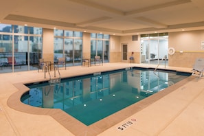 Una piscina interior con agua cristalina, líneas de profundidad marcadas y una silla de socorrista.