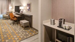 A hotel room with a desk, chair, and a coffee machine.