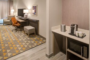 A hotel room with a desk, chair, and a coffee machine.