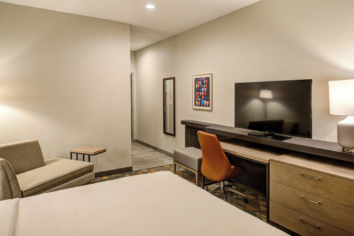 A hotel room with a bed, a desk, a chair, a television, and a small table.