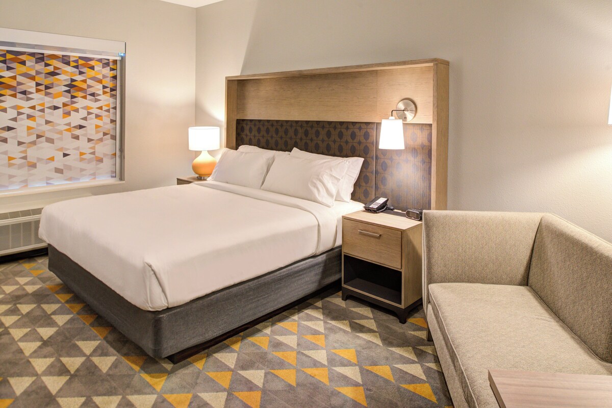 A hotel room with a bed, bedside table, lamp, and a sofa.