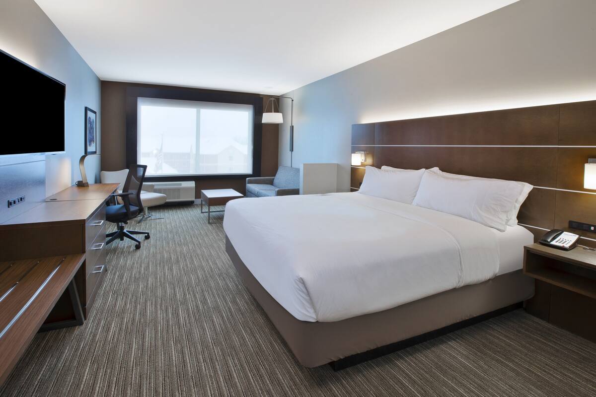 A hotel room with a large bed, a desk with a computer, a chair, and a TV.