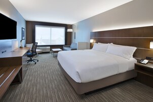 Habitación de hotel con una cama grande, un escritorio con computadora, una silla y un televisor.