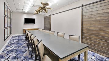 Ein Konferenzraum mit einem langen Tisch, Stühlen, einem Flachbildfernseher und einer Wand mit Holzverkleidung.
