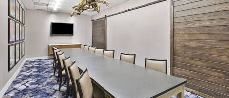 A conference room with a long table, chairs, a flat-screen TV, and a wooden panel wall.