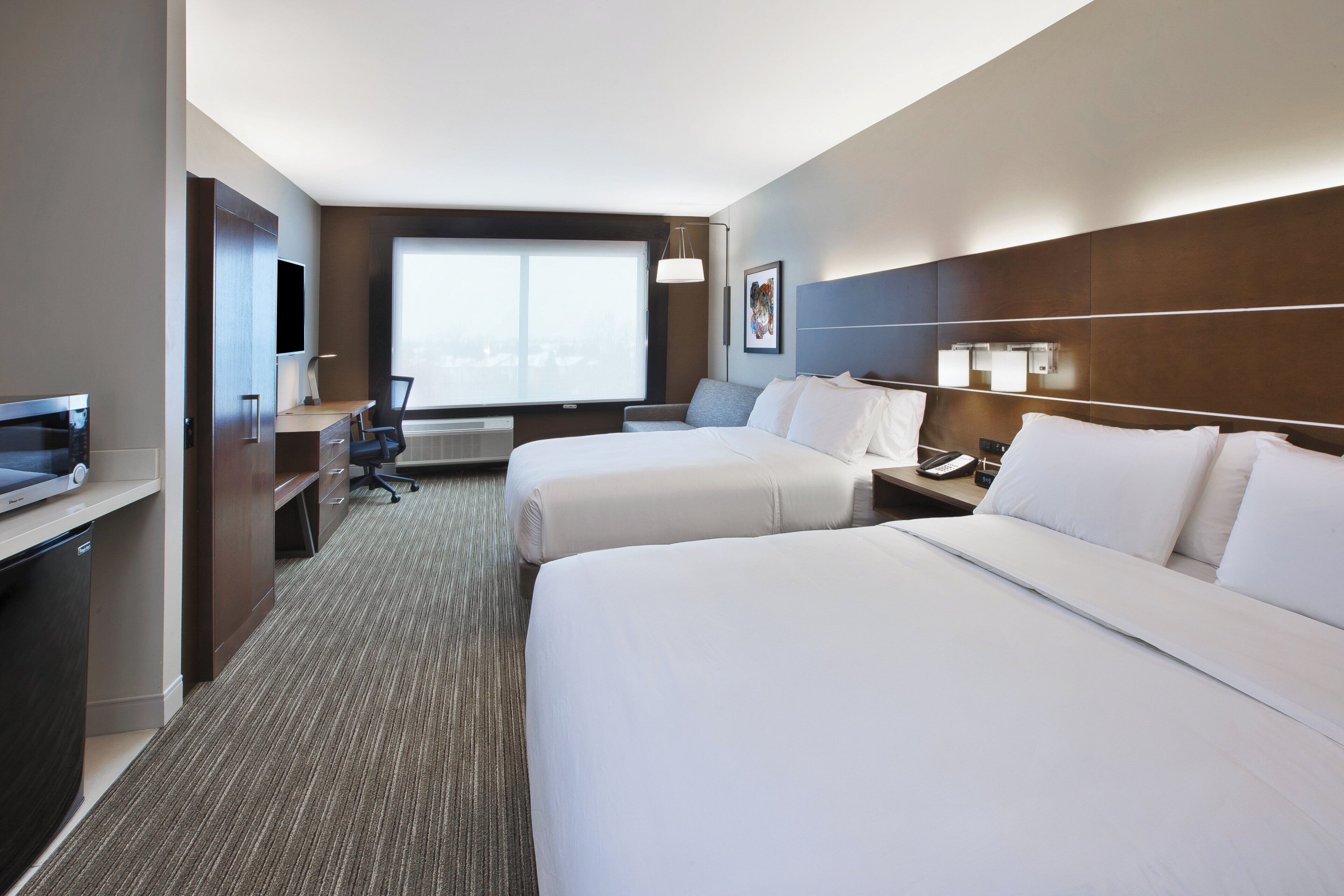 A hotel room with two beds, a desk, a chair, a television, and a window.