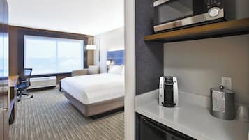 A hotel room with a bed, desk, chair, kitchenette, and a large window.
