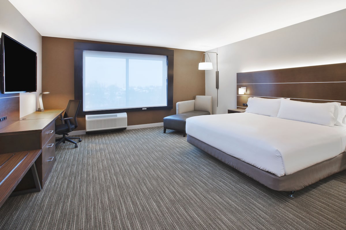 A hotel room with a large bed, a desk with a chair, a TV, and a window with a city view.