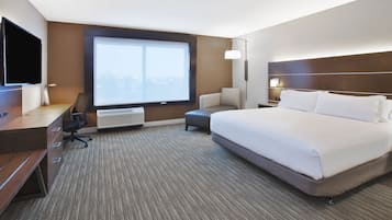 A hotel room with a large bed, a desk with a chair, a TV, and a window with a city view.