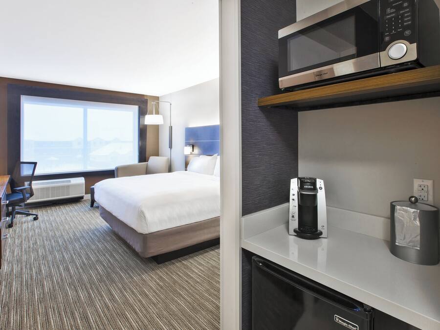 Een hotelkamer met een bed, bureau, stoel, kitchenette en een groot raam.