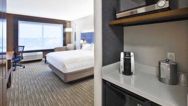 A hotel room with a bed, desk, chair, microwave, coffee maker, and a view of the mountains. - Holiday Inn Express & Suites Okemos - University Area by IHG (Okemos)