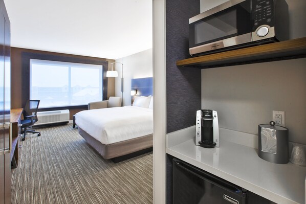 A hotel room with a bed, desk, chair, microwave, coffee maker, and a view of the mountains. - Holiday Inn Express & Suites Okemos - University Area by IHG (Okemos)
