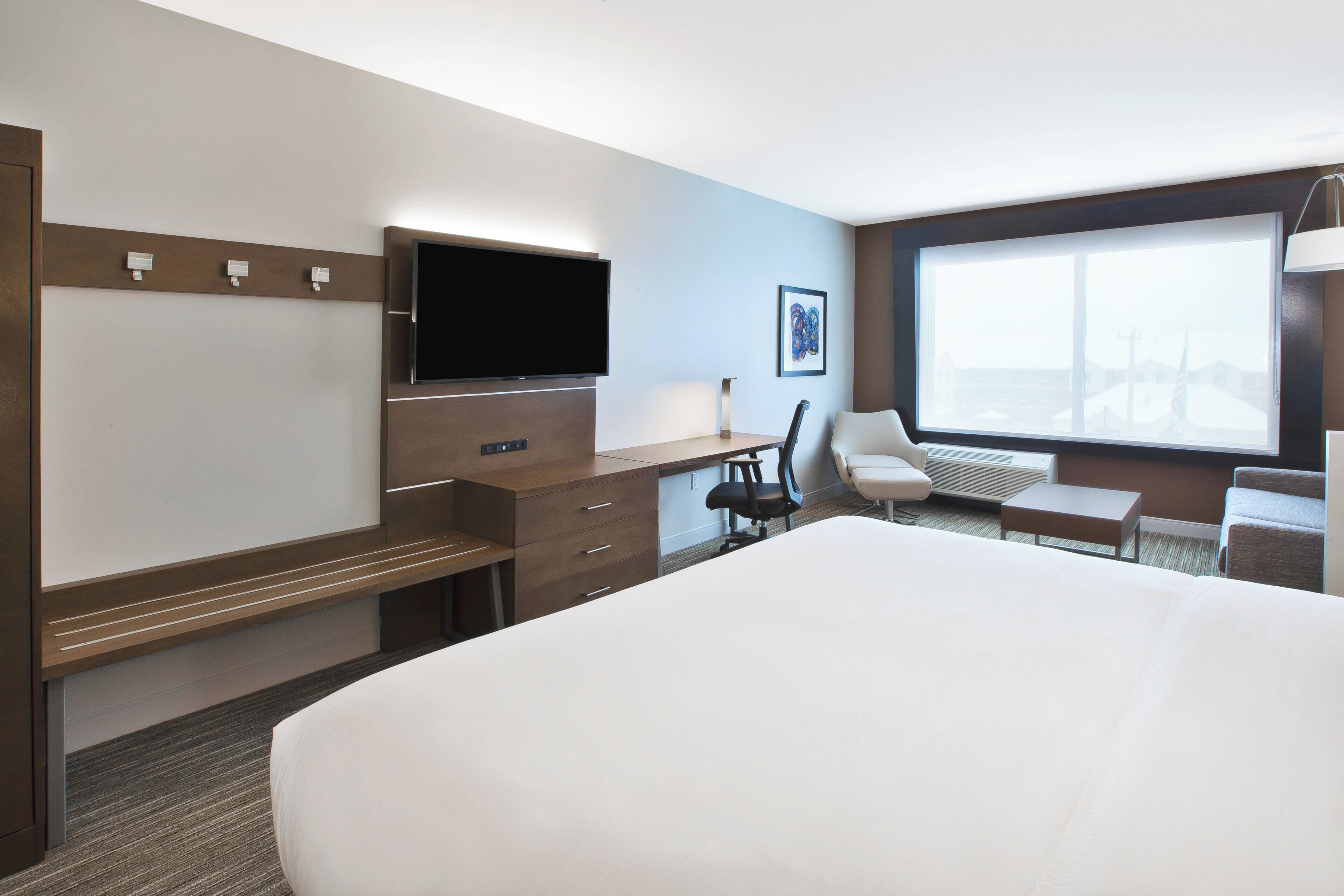 A hotel room with a bed, a desk, a chair, a TV, and a large window.