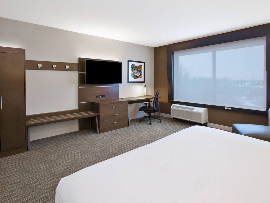 Quarto de hotel com uma cama grande, uma escrivaninha com cadeira, televisão e janela com vista exterior.