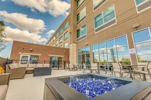 An outdoor seating area with a fire feature, a brick building, and a glass facade. - Holiday Inn Express & Suites Okemos - University Area by IHG (Okemos)