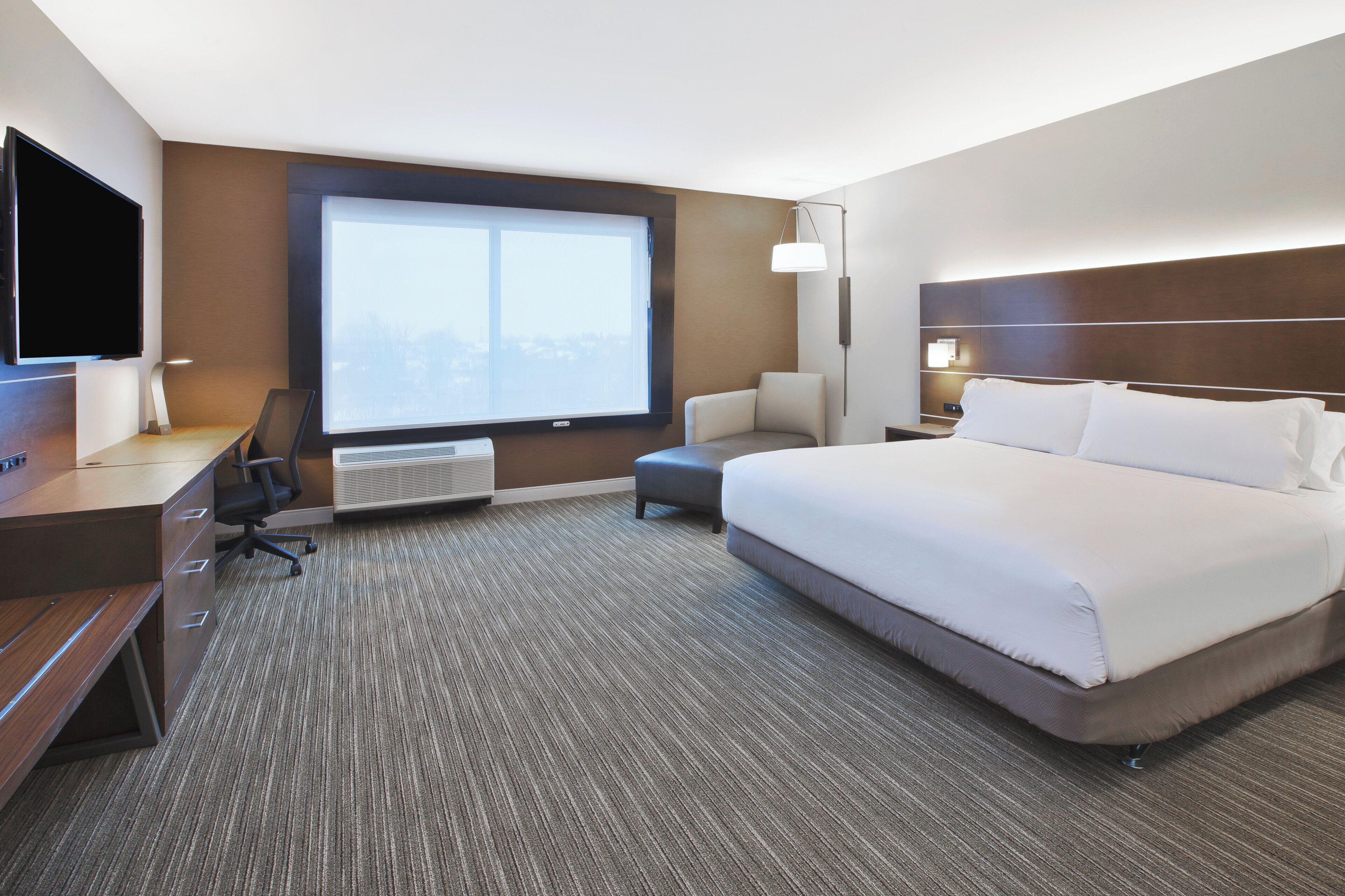A hotel room with a large bed, a desk with a chair, a TV, and a window with a view.