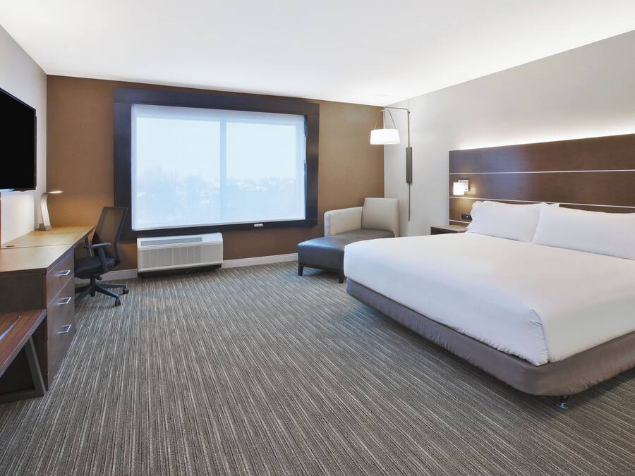 A hotel room with a large bed, a desk with a chair, a TV, and a window with a view.