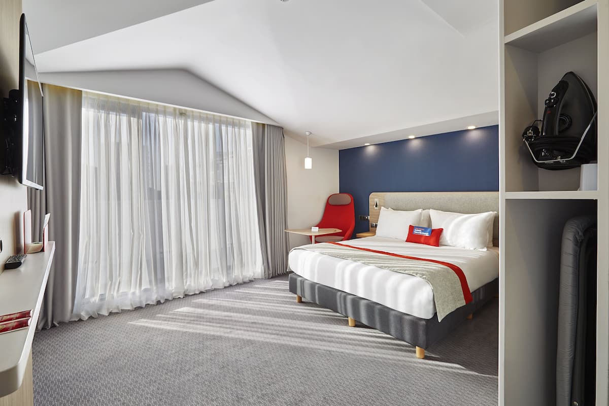 A modern hotel room with a large bed, a desk, a chair, and a TV.