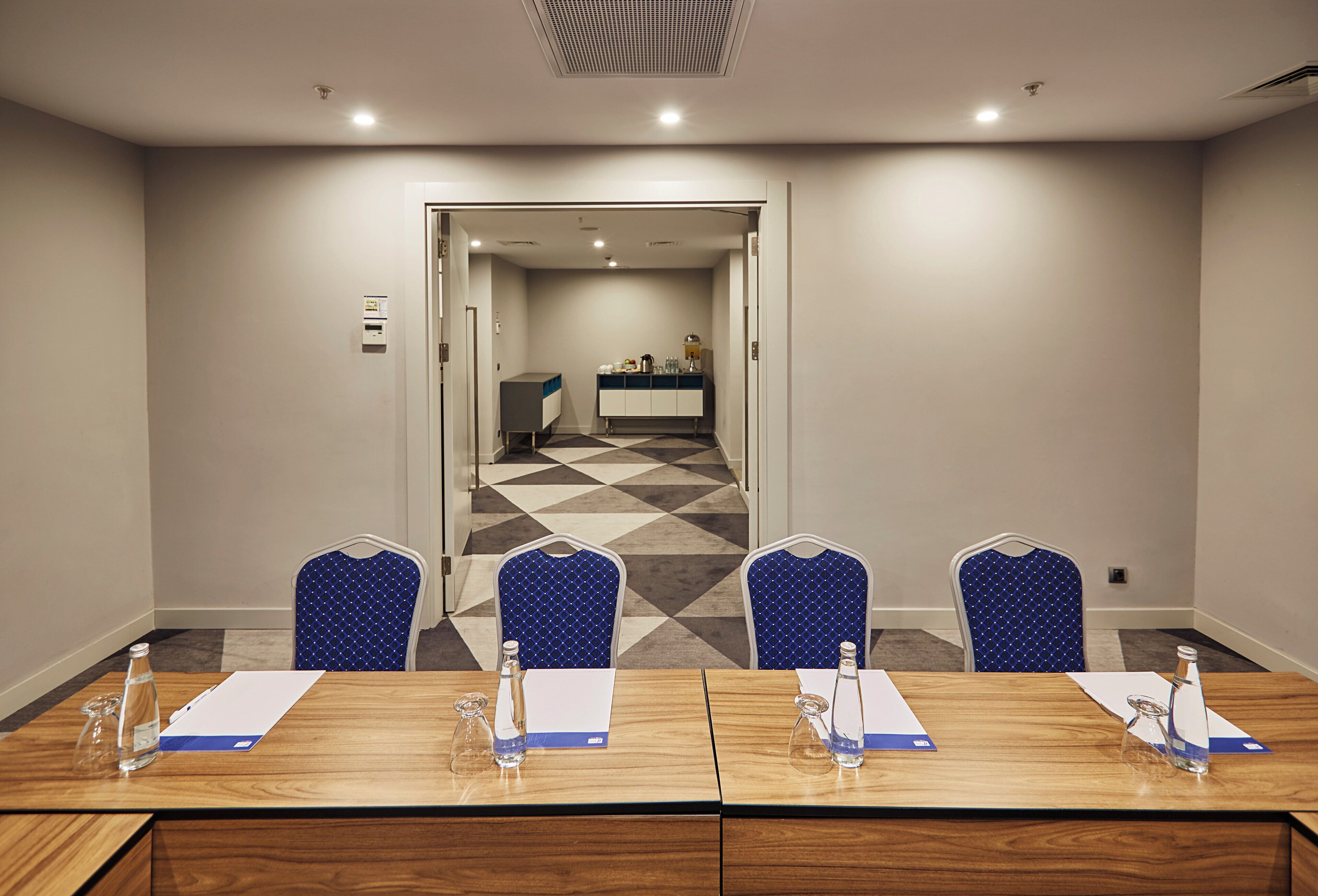 Un salón de conferencias con una mesa larga, cuatro sillas y una kitchenette al fondo.