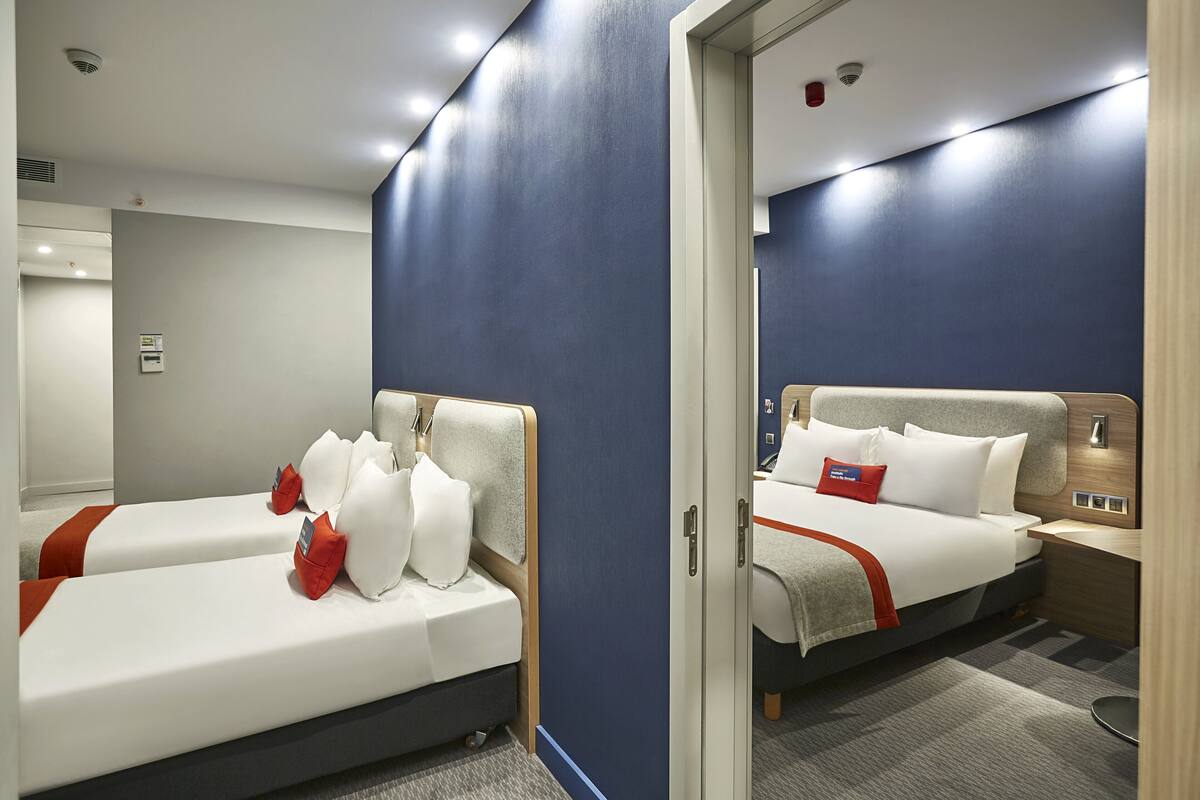 A hotel room with two beds, a mirror, a nightstand, and a wall-mounted light.