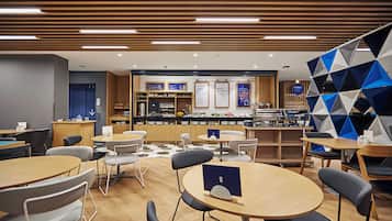 A modern cafe with round tables and chairs, a counter with a menu, and a geometric wall decoration.