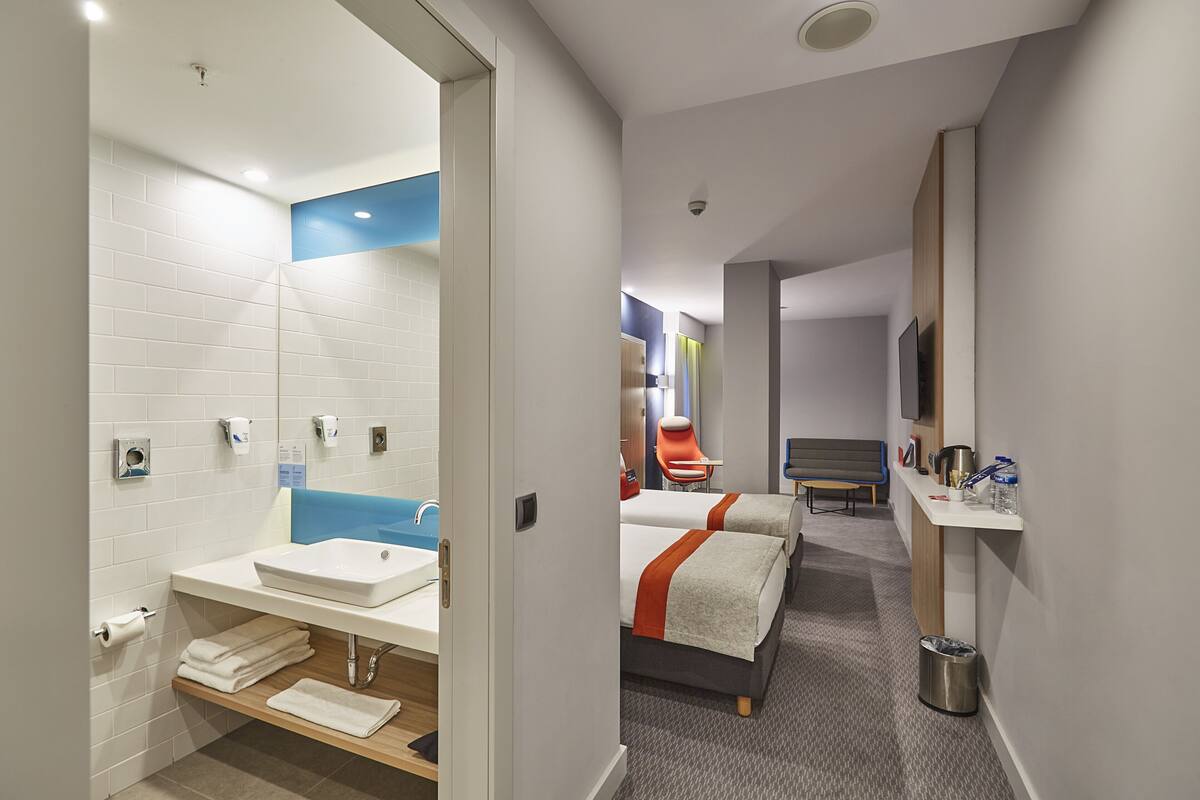A hotel room with a bathroom, a bed, a TV, and a desk.