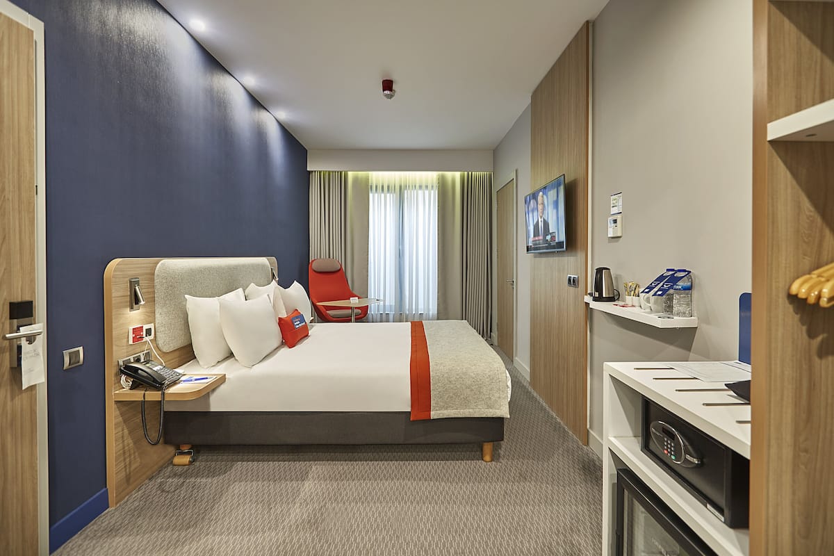 A hotel room with a bed, a desk with a phone, a TV, and a minibar.