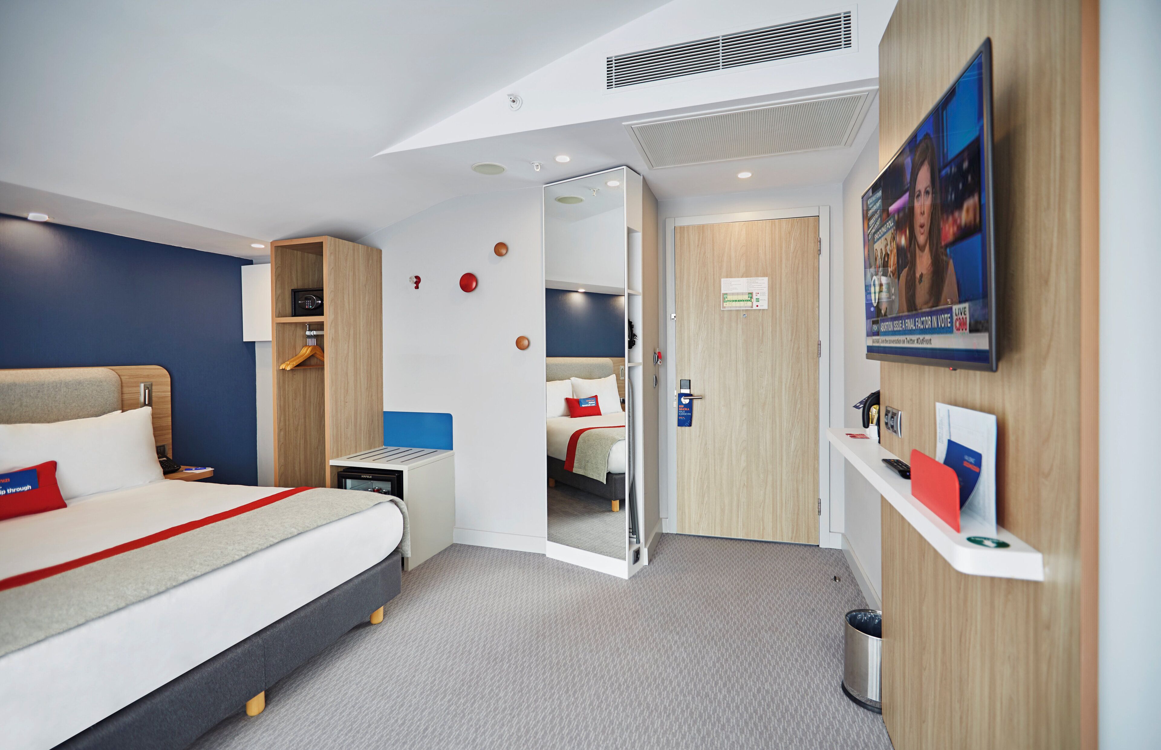 Una habitación de hotel moderna con cama, escritorio, espejo, armario y televisor.