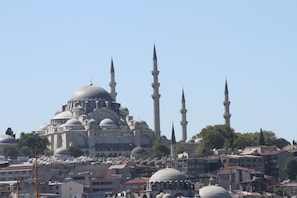 A historic building with multiple domes and minarets, surrounded by urban structures.