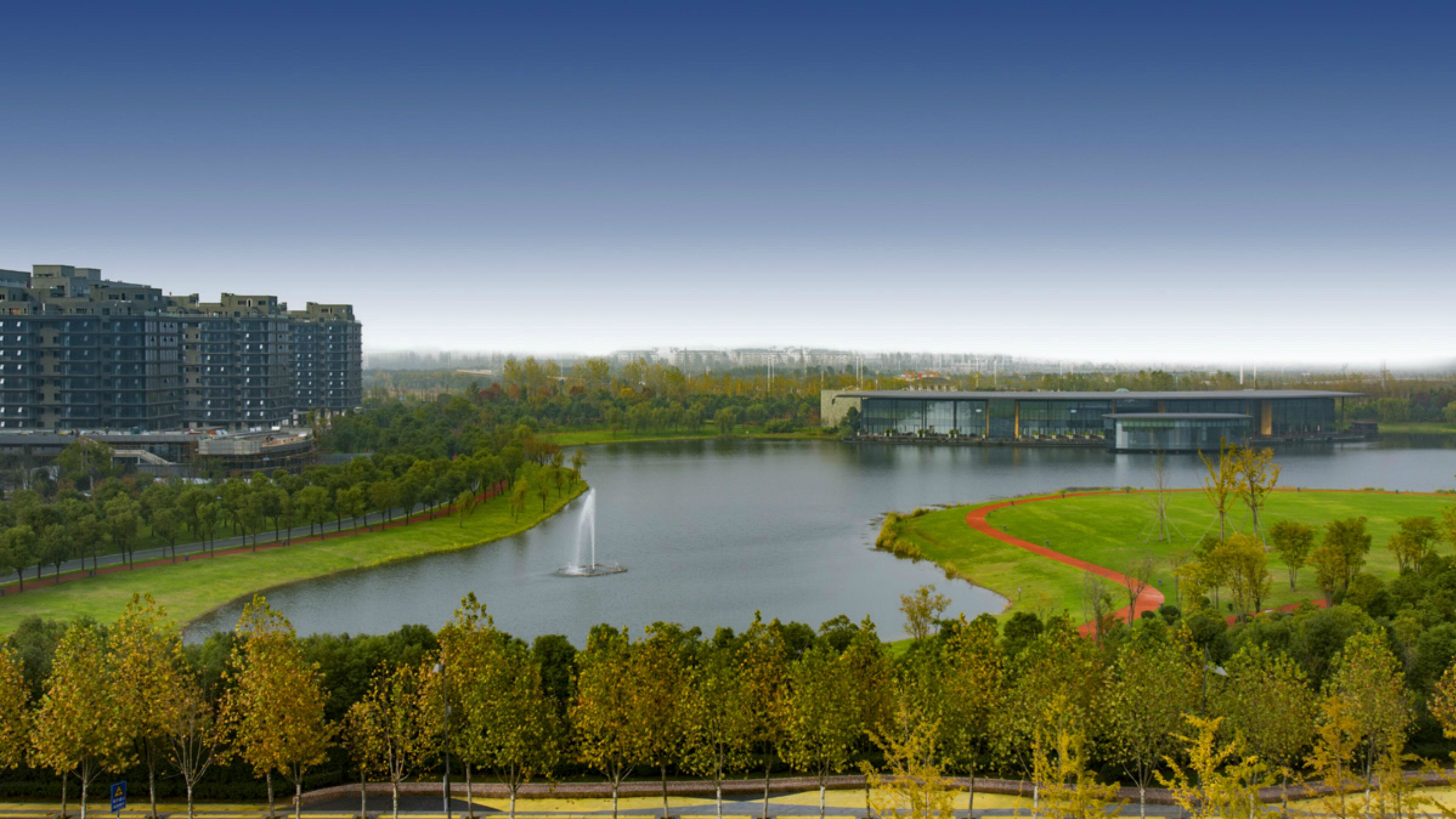 A large body of water with a fountain, surrounded by greenery and modern buildings.