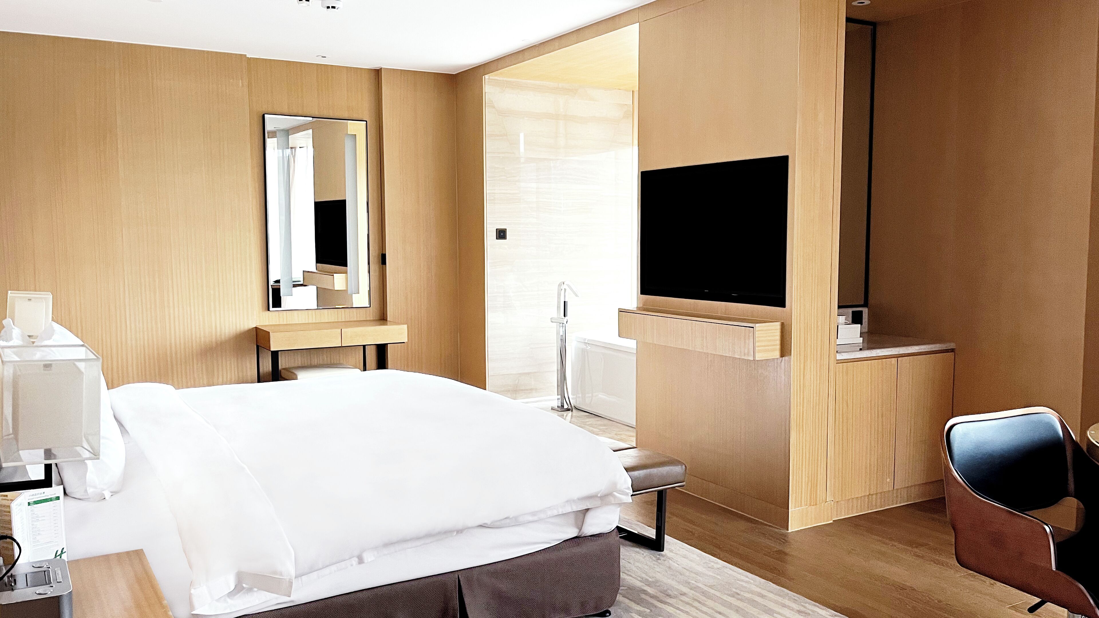 A hotel room with a bed, a desk, a chair, a TV, and a mirror.