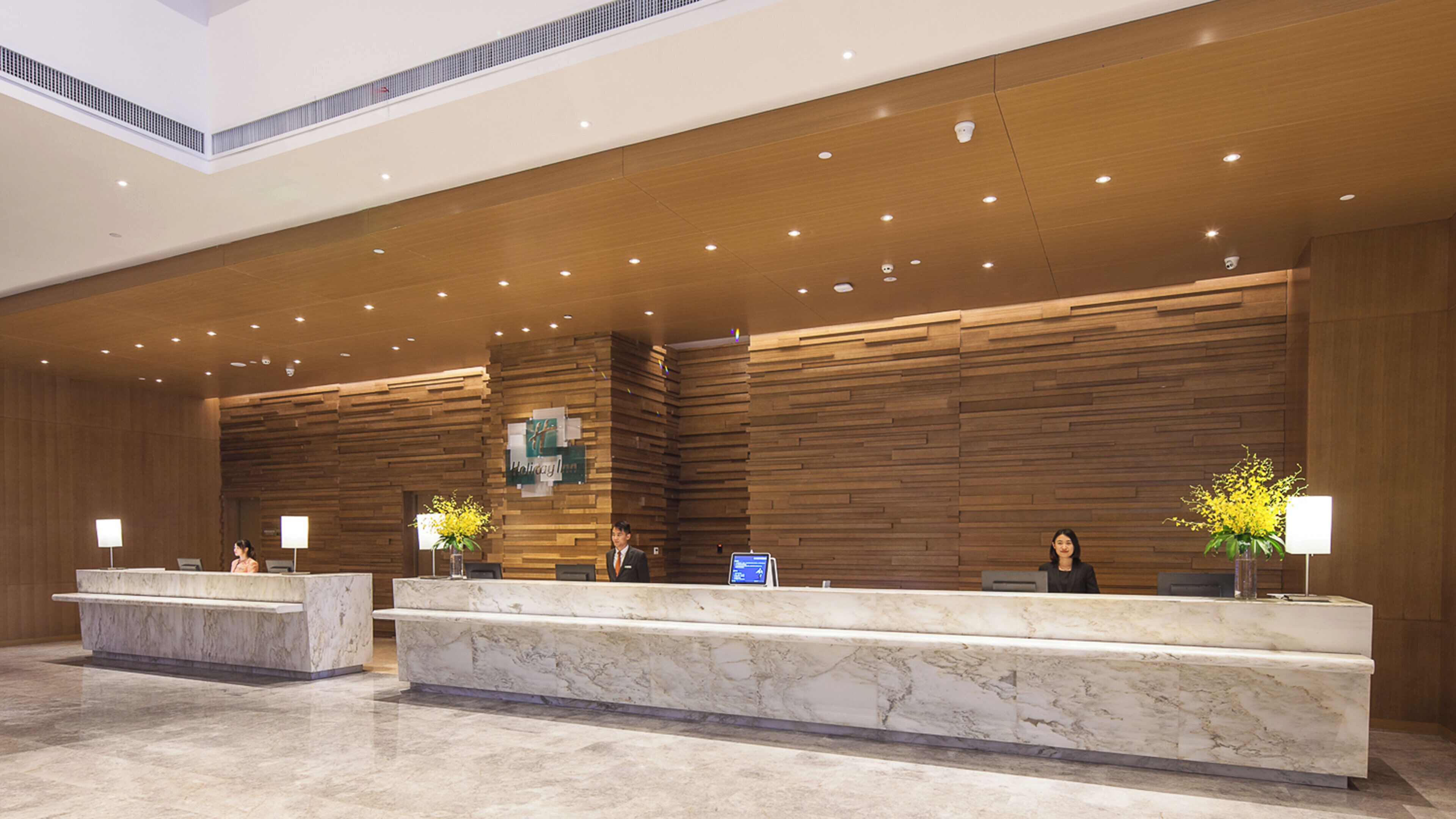 A hotel reception area with marble counters, wooden paneling, and a high ceiling with recessed lighting.
