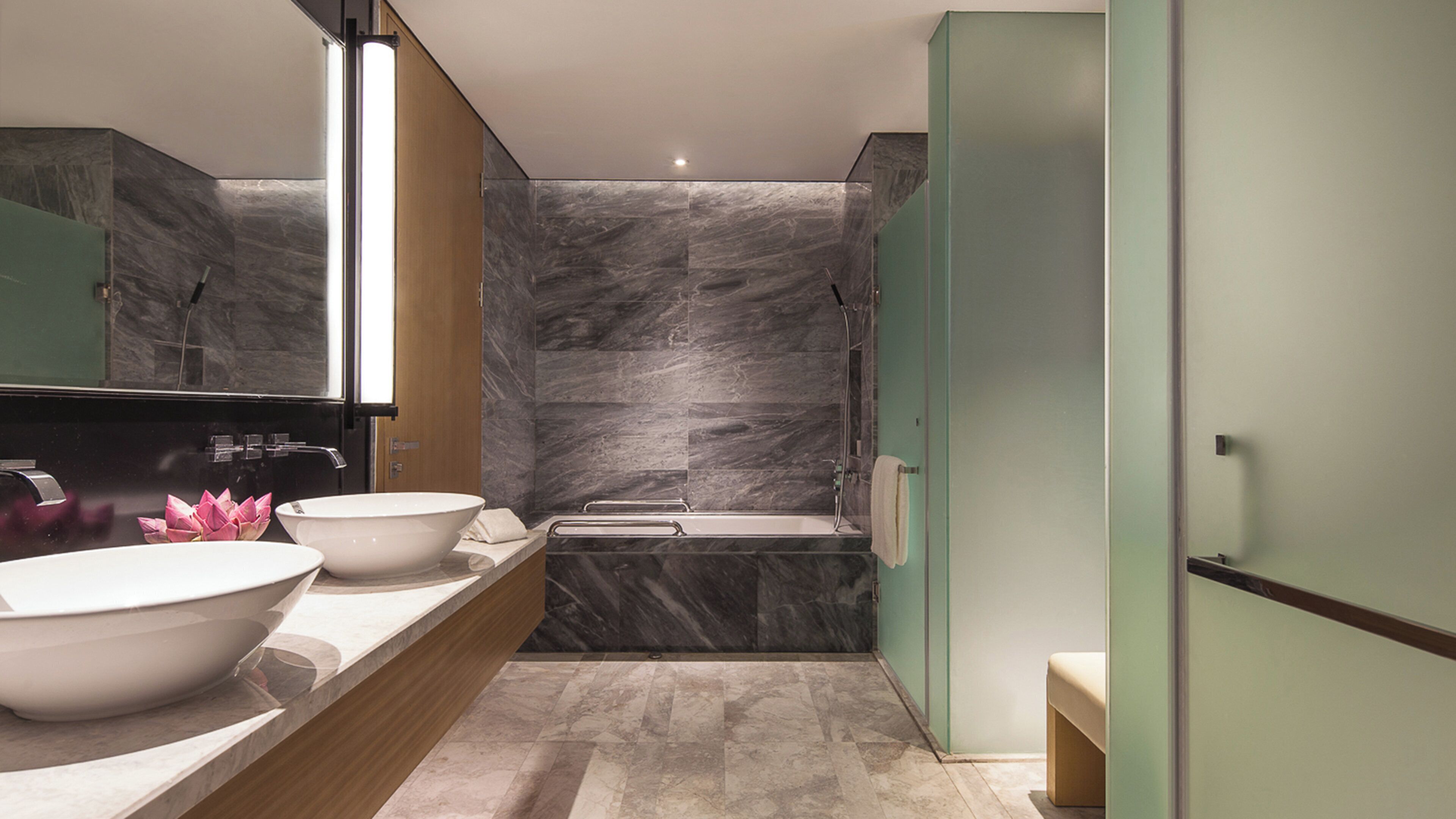A modern bathroom with a large mirror, two sinks, a bathtub, and a shower.