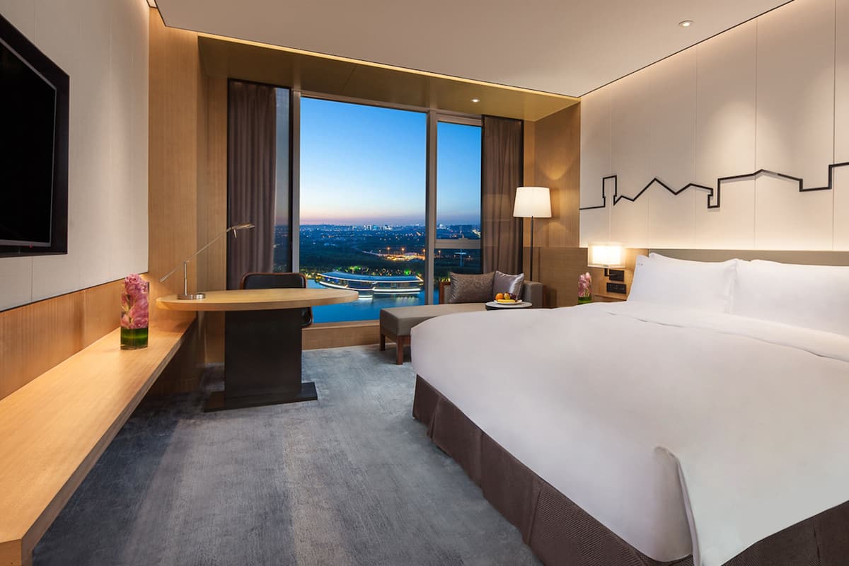 Een moderne hotelkamer met een groot bed, een bureau en uitzicht op een stadsgezicht.